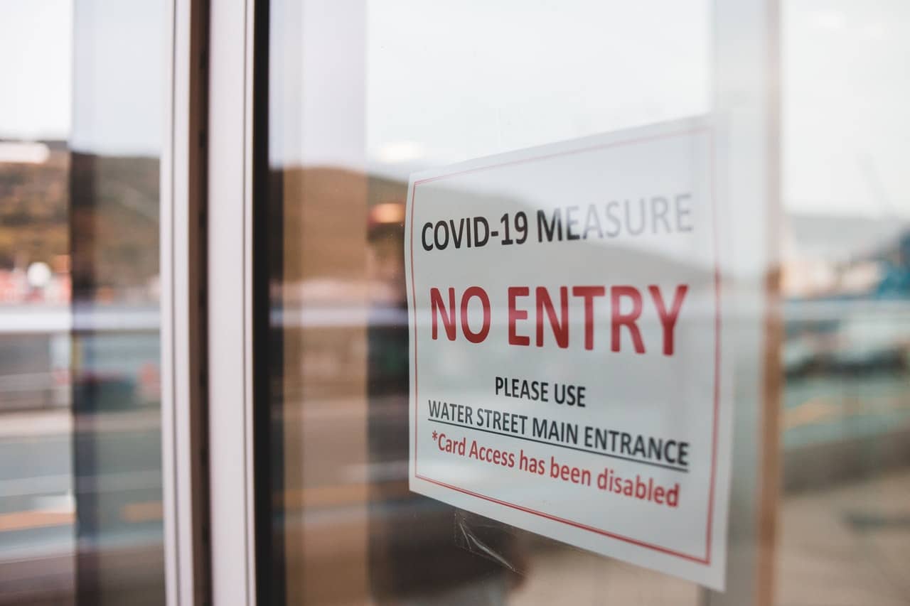 COVID sign limiting entrances in a public building representing the limitation of liability for COVID exposure to Ontario businesses