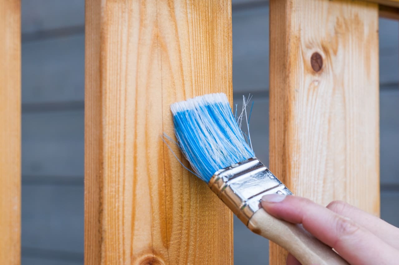 A person staining a fence representing how to resolve fence disputes between neighbours