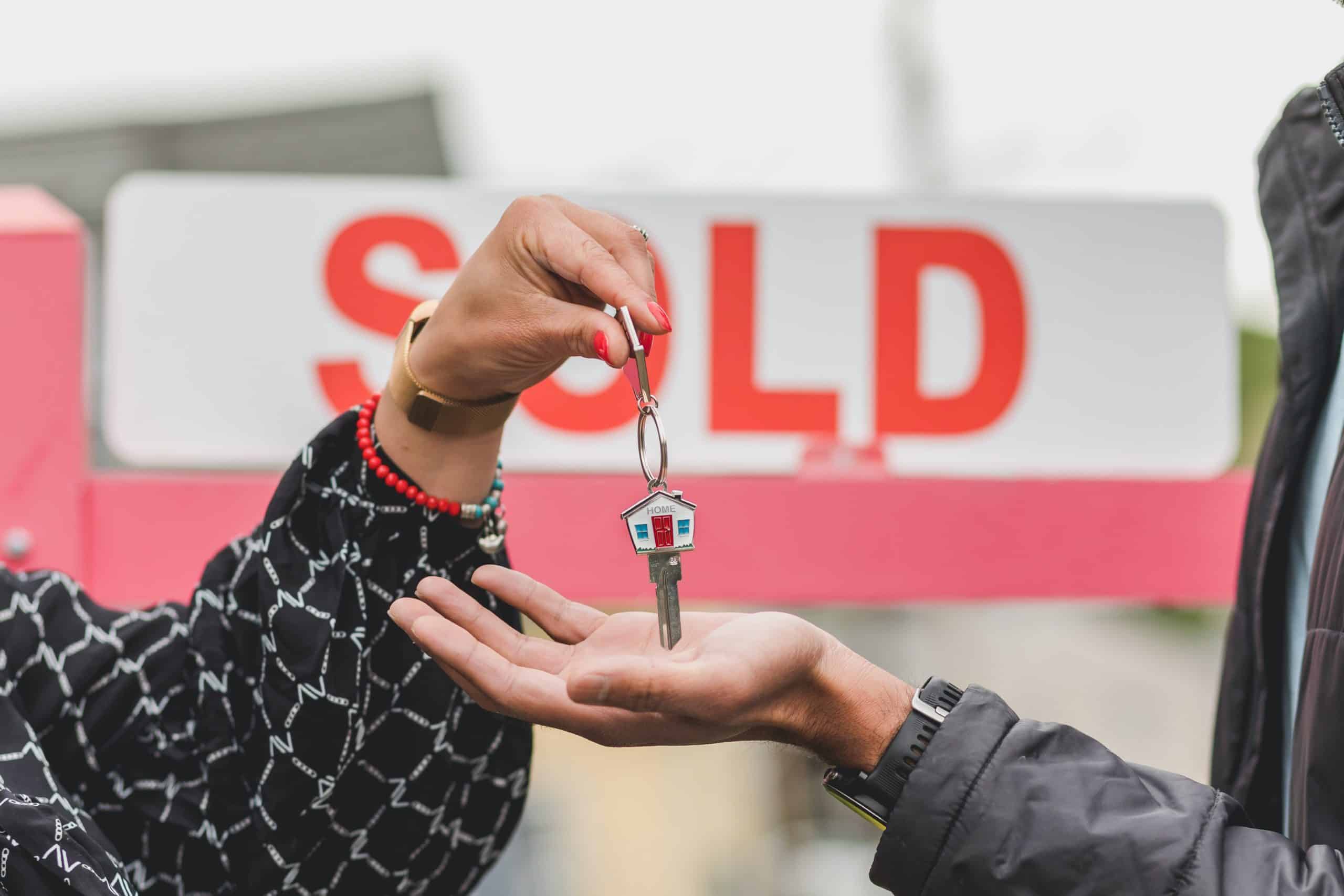 a person holding a set of keys in front of sold sign