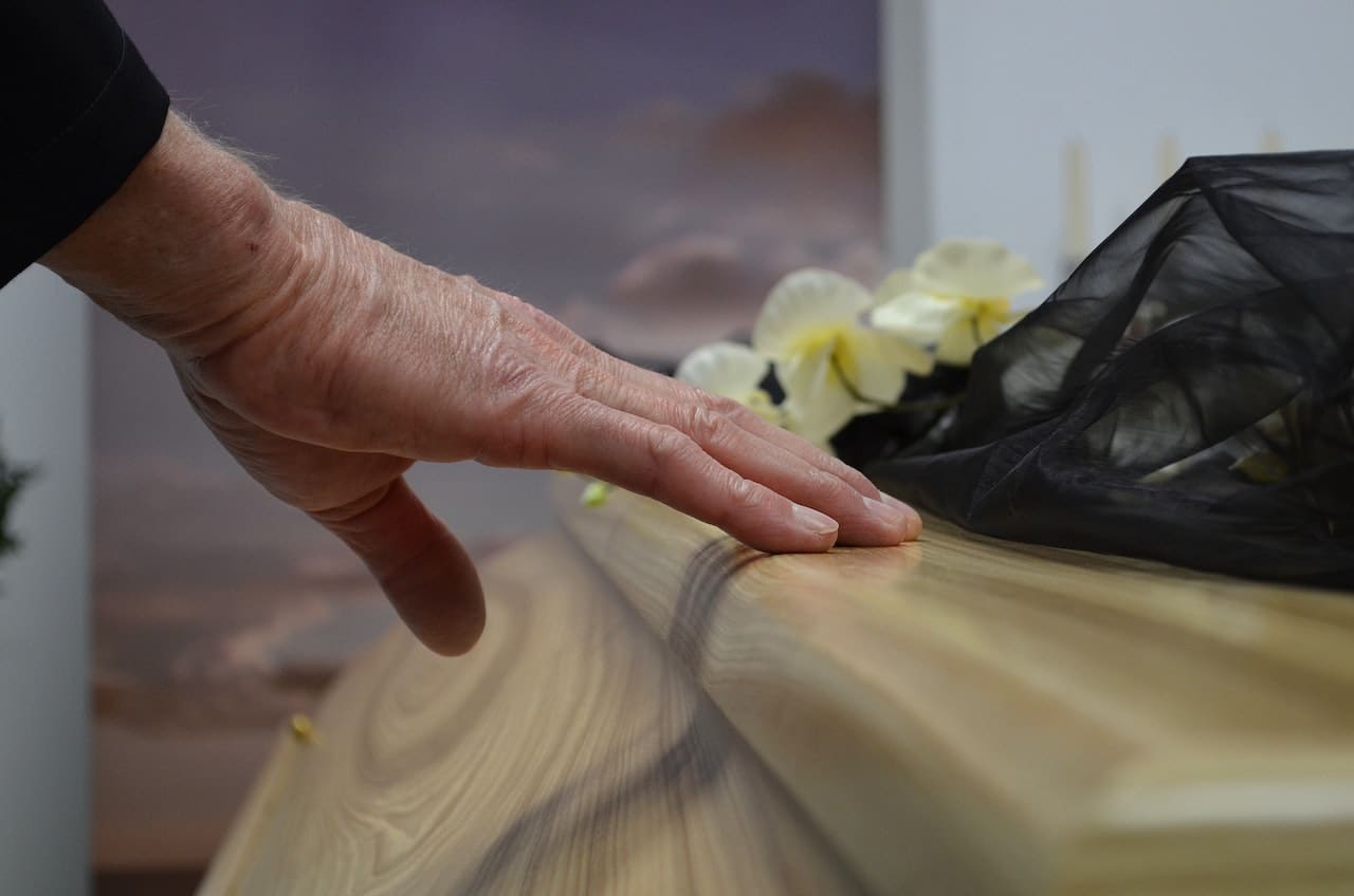 a person touching a wood coffin