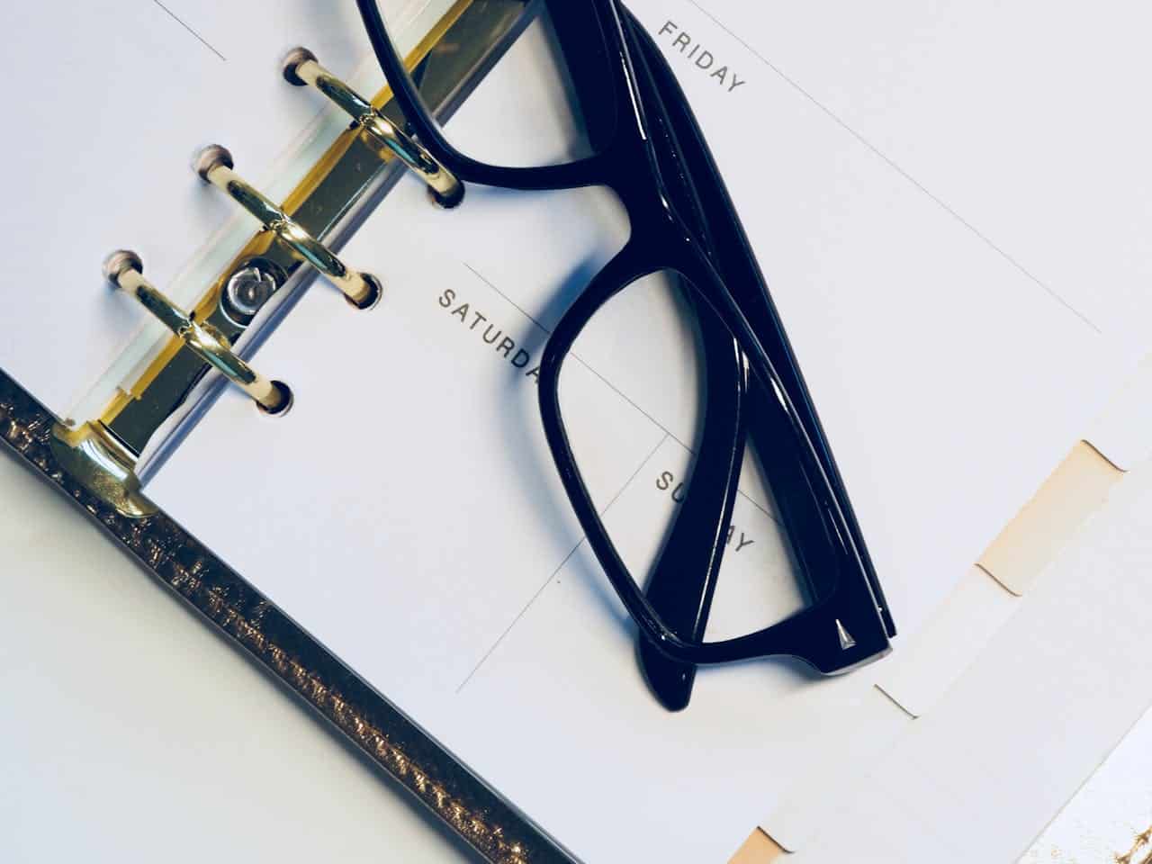 black framed glasses sitting on a calendar agenda book
