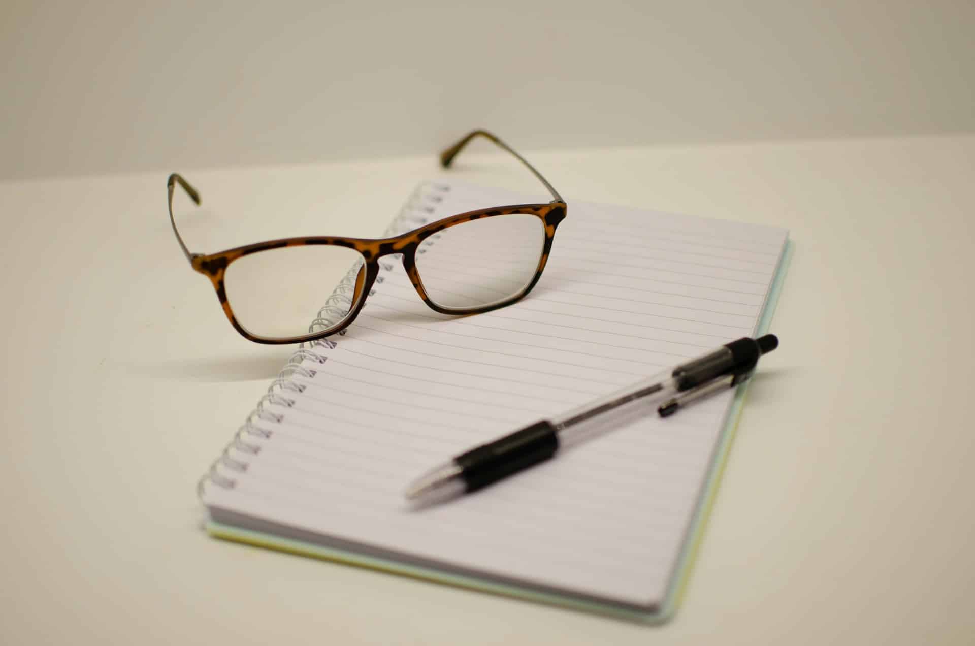 a pair of glasses a pen and notepad
