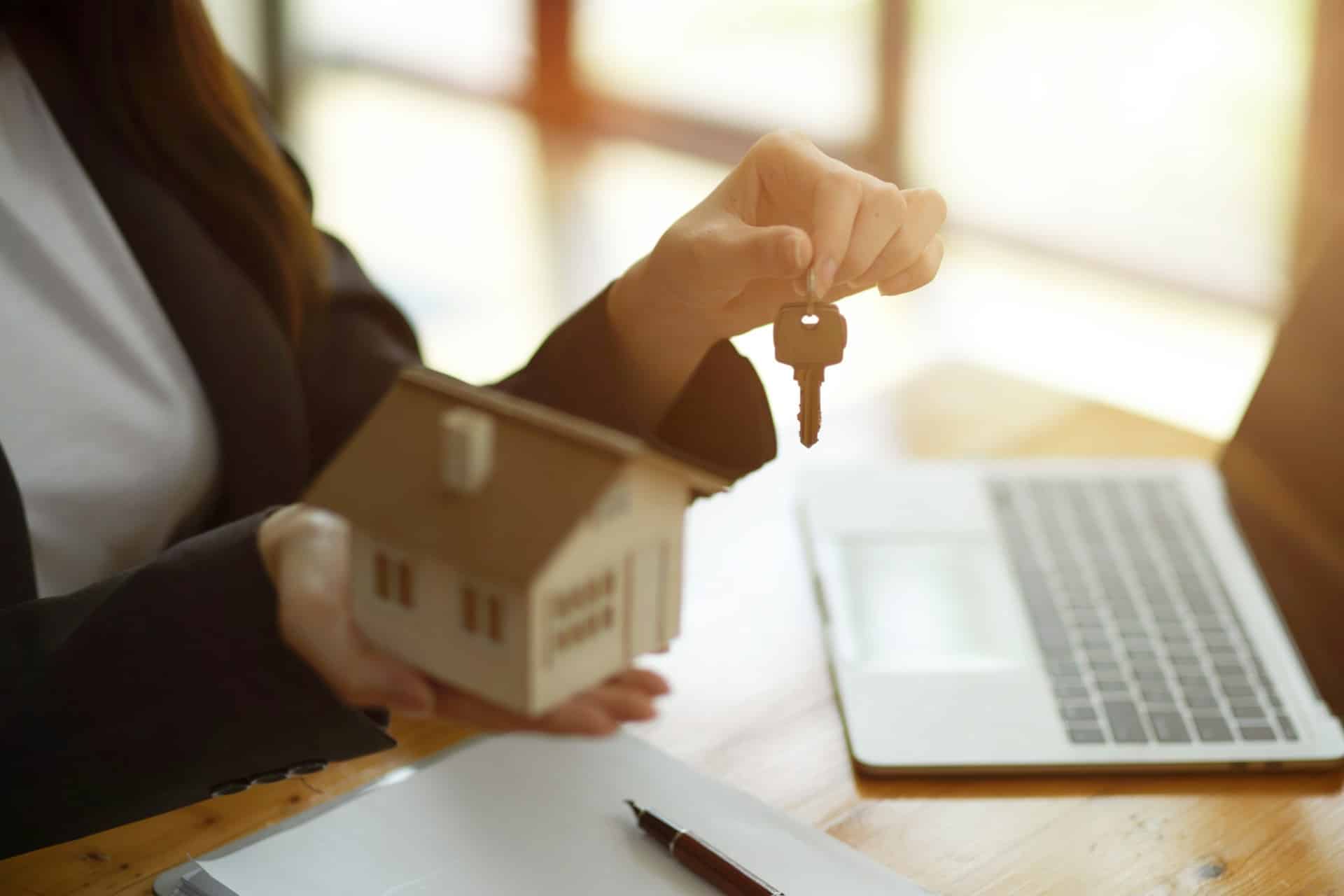 A woman sitting behind a laptop holding a key in one hand and a model house in the other, representing private mortgages.