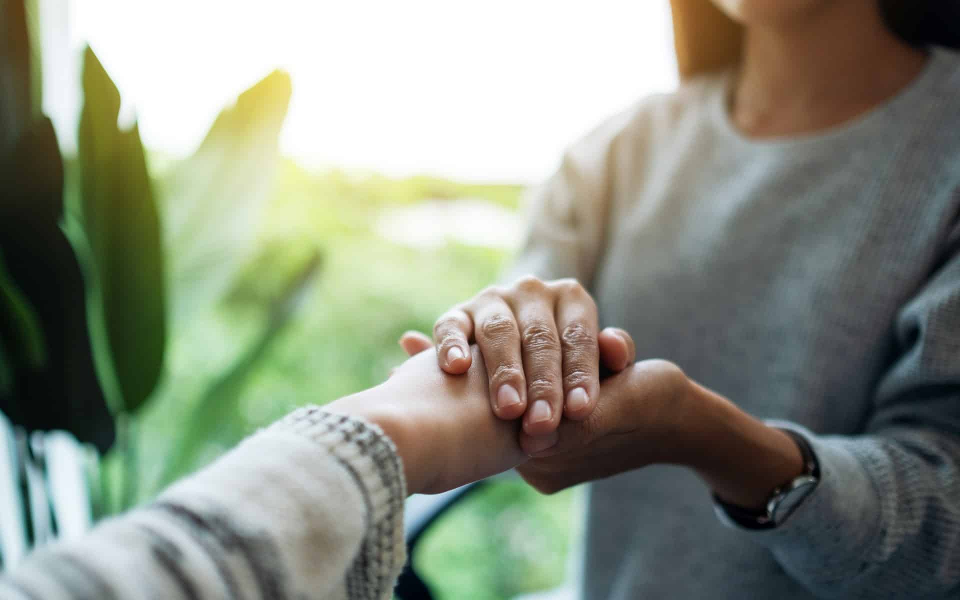 A woman holding the hand of another person, representing trauma-informed.