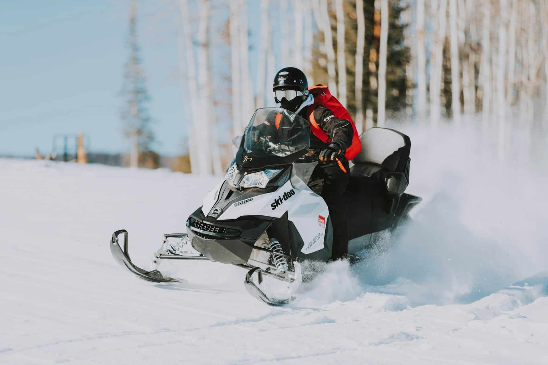 A snowmobile kicks up a cloud of snow behind it as a masked driver, wearing a black helmet, speeds across a snow-covered field with blurred trees in the background, representing snowmobile accidents in Ontario.