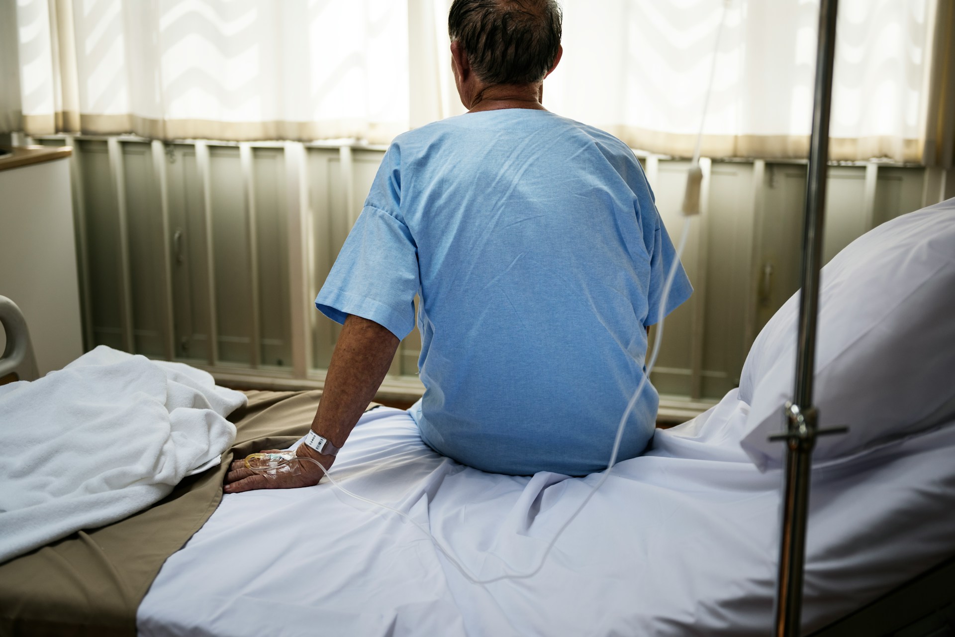 An elderly man sitting on a hospital bed facing the window with a soft glow of light representing elderly personal injuyr claims in Ontario.