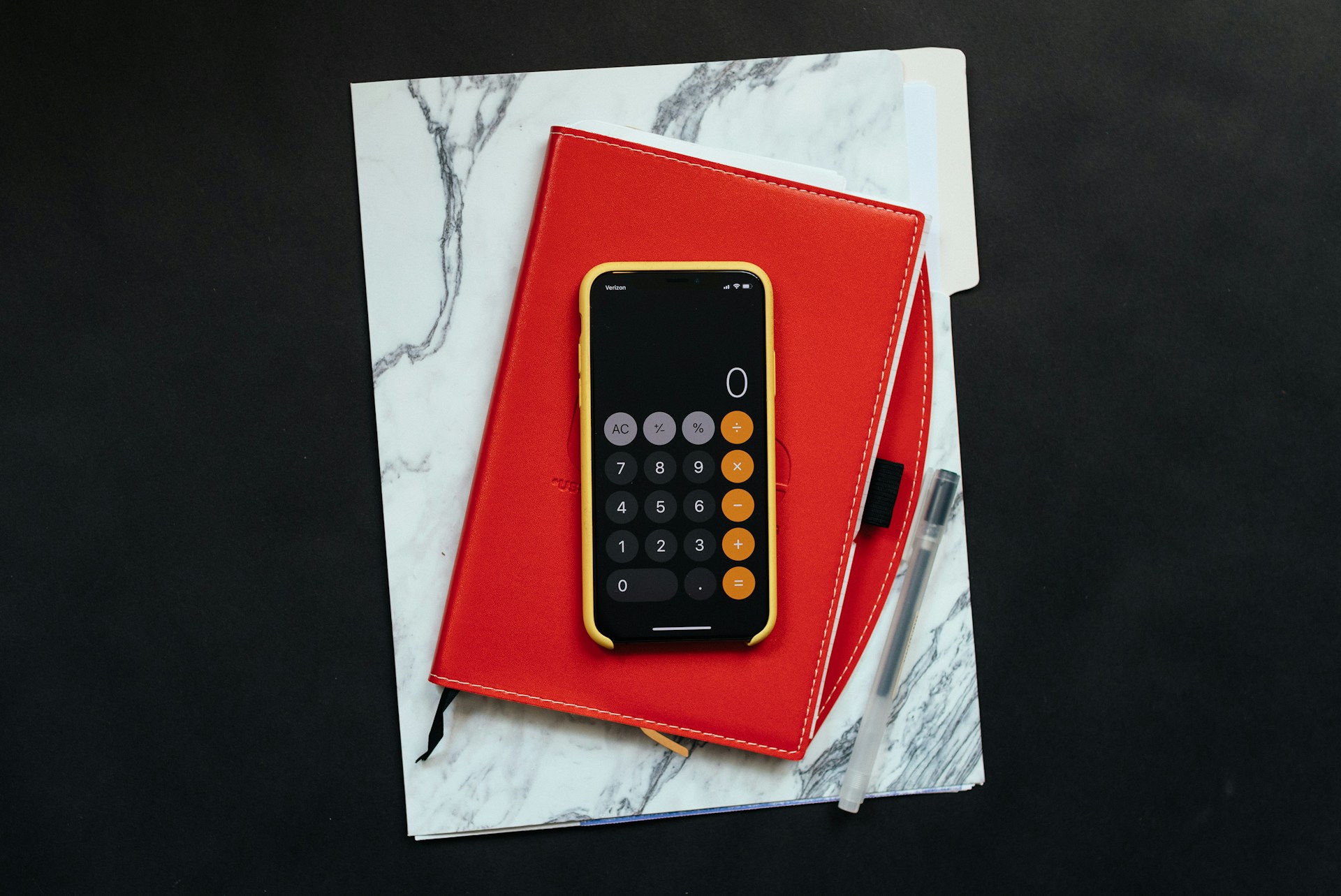 Black smartphone sitting on a red folder with a pen representing income loss for self-employed injury claims in Ontario.