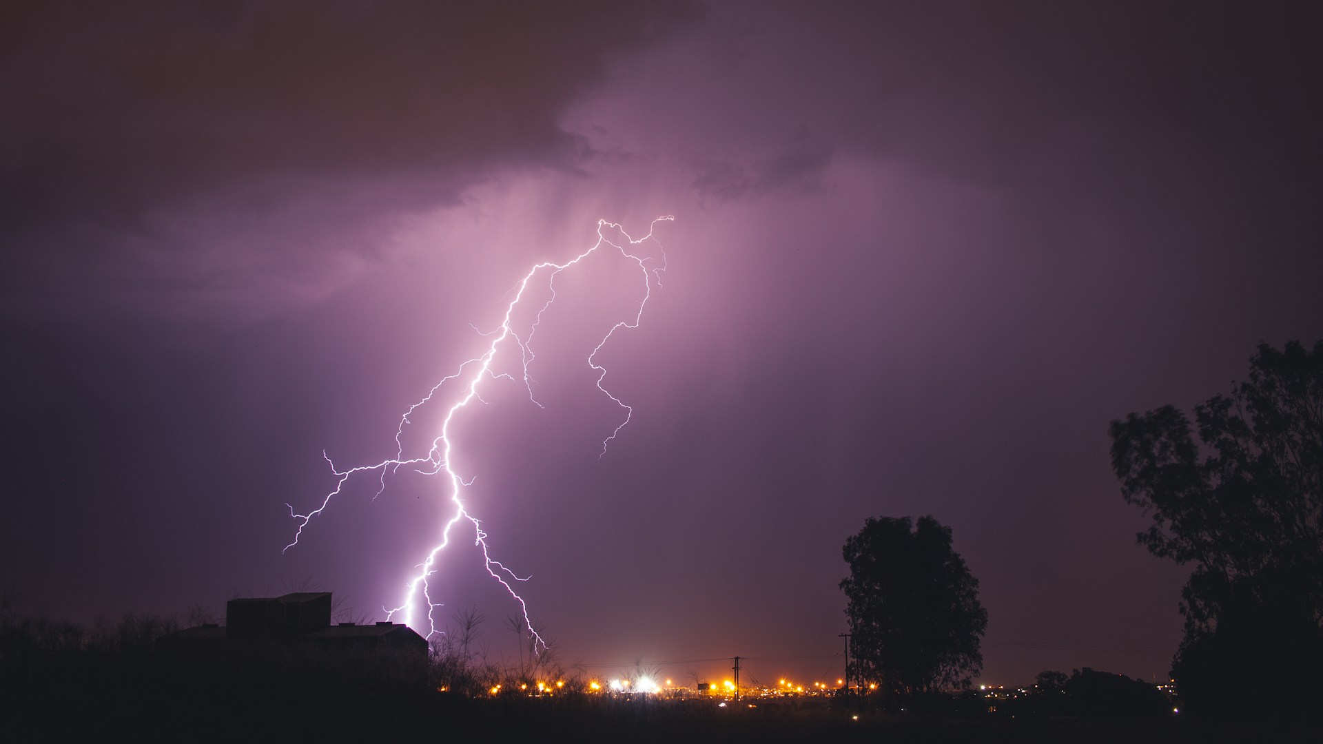 Purple lightning lights up a cloudy sky at night over the lights of a residential area, representing Ottawa storm, flooding, and insurance claims.